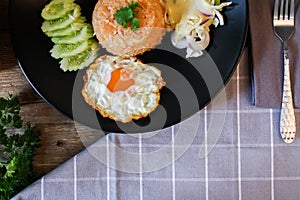 Fried rice, fried egg, cucumber, sliced tomato, green salad and Fried chicken placed on a black plate as a garnish