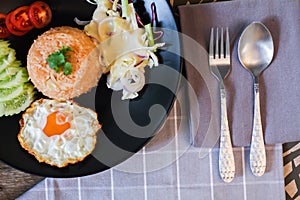 Fried rice, fried egg, cucumber, sliced tomato, green salad and Fried chicken placed on a black plate as a garnish