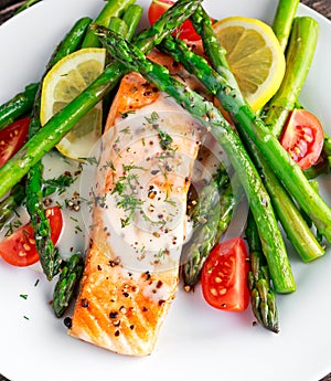 Fried salmon with asparagus, tomatoes, lemon, yellow lime on white plate