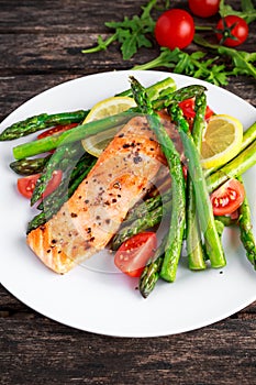 Fried salmon with asparagus, tomatoes, lemon, yellow lime on white plate