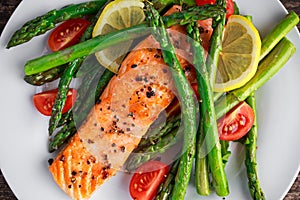 Fried salmon with asparagus, tomatoes, lemon, yellow lime on white plate