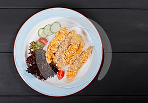 Fried salmon fillet with vegetables salad on black plate on dark background.