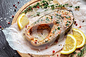 Fried salmon steak with thyme and lemon served on wooden plate on black table