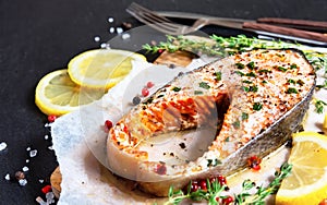 Fried salmon steak with thyme and lemon served on wooden plate on black table