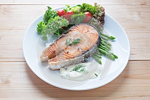 Fried salmon with vegetable on a round white plate on wooden background