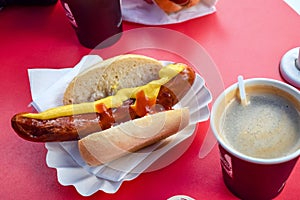 Fried sausage in a bun with mustard and ketchup with coffee in a cafe