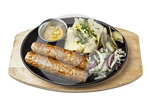 Fried sausages with mashed potatoes, pickles and mustard sauce served on a cast-iron frying pan. Appetizing traditional lunch.
