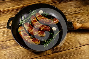 Fried sausages with rosemary, garlic and spices in cast iron grill frying pan on wooden table