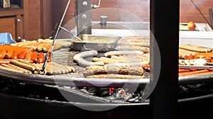 Fried sausages. Street eatery. Many grilled sausages on a large round barbecue grill at a street food festival. Barbecue