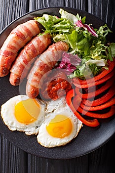 Fried sausages wrapped in bacon, eggs and fresh salad close-up.