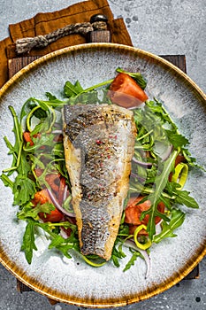 Fried sea bass fillet with vegetable salad, Dicentrarchus fish. Gray background. Top view