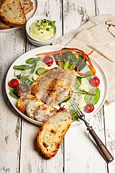 Fried sea fish and vegetables. Tilapia fillet with broccoli, cherry tomatoes and lettuce. Sea food on a white plate