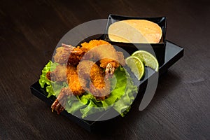 Fried shrimp in batter with sauce, salad leaves and lemon on a black chalkboard