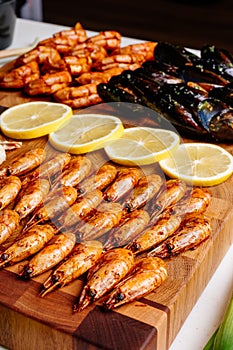 Fried shrimps and fried mussels with sauce and fried langoustines and sliced lemon on wooden cutting board and jacinths