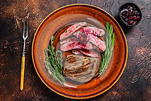 Fried sliced flank or bavette beef meat steak on a plate. Dark background. Top view