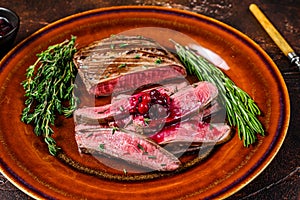 Fried sliced flank or bavette beef meat steak on a plate. Dark background. Top view