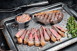 Fried and sliced Top sirloin steak, Grilled cup rump beef meat steak on a steel serving tray with spices. Black