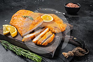 Fried sliced weiner schnitzel on a wooden board with herbs. Black background. Top view