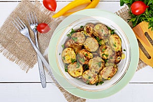 Fried slices of young zucchini with hot pepper, greens on a plate on a white wooden background.