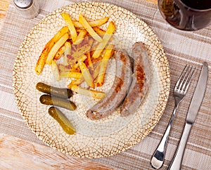 Fried small sausage and french fries, completed with pickled gherkin cucumber