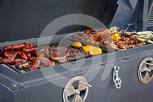 Fried smoked sausages, fried chicken wings, peppers and paprika, toasted corn on fire, street food, mobile barbecue, trailer on wh