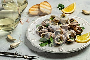 Fried snails Escargots de Bourgogne with herbs, butter, garlic on metal plate with forks, wine glass. gourmet food