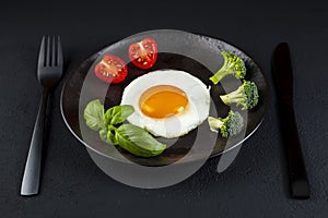 Fried soft-boiled egg on a black plate with fresh vegetables