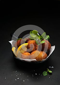 Fried Spanish bacalao croquettes in iron pan made with breaded salted codfish and served as traditional tapas or snacks. Dark