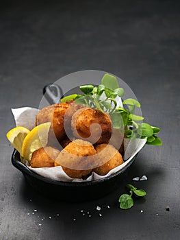 Fried Spanish bacalao croquettes in iron pan made with breaded salted codfish and served as traditional tapas or snacks. Dark