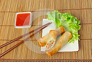 Fried spring rolls, one cut, on a plate with chopsticks