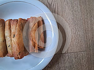 Fried spring rolls on a white plate with a wooden background