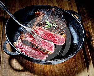 Fried steak with rosemary and spices in a pan, fork on a wooden background