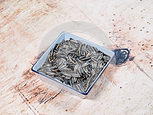 Fried sunflower seeds in a white ceramic bowl on wooden background