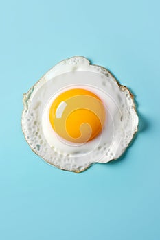 Fried sunny-side-up egg with bright yellow glossy yoke on light blue background. Culinary food concept