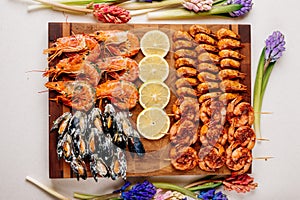 Fried tails of langoustines and fried mussels with sauce and fried shrimps and sliced lemon on wooden cutting board and jacinths