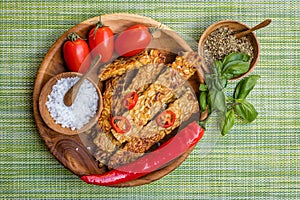 Fried tempeh, chili peppers, fresh cherry tomatoes, basil leaves, mix of herbs and sea salt in wooden pots with wooden spoons on a