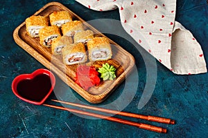 Fried tempura sushi rolls set on wooden plate on dark background. Japanese traditional fusion food style, restaurant