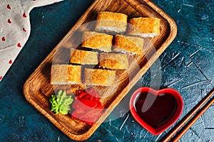 Fried tempura sushi rolls set on wooden plate on dark background. Japanese traditional fusion food style. Top view