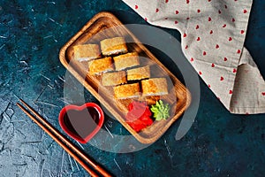 Fried tempura sushi rolls set on wooden plate on dark background. Japanese traditional fusion food style. Top view