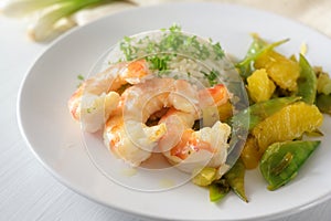 Fried tiger prawn shrimp dish with sugar peas, onion and oranges served with rice and parsley garnish on a white plate, selected