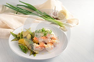 Fried tiger prawn shrimp dish with sugar peas, onion and oranges served with rice on a white table, copy space