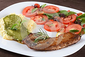 fried tilapia fish filet served on plate with tomato salad and mashed potatoes with herb pesto