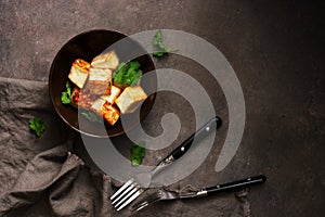 Fried tofu cheese in a bowl with greens on a dark background. Top view, copy space