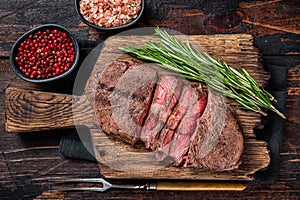 Fried Top Blade or flat iron roast beef meat steaks on wooden board with rosemary. Dark wooden background. Top View