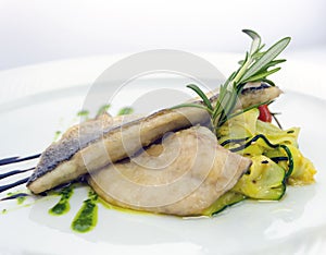 Fried trout with fresh cucumbers, pickled tomatoes and a rosemary branch on a white plate