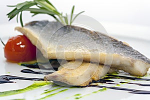 Fried trout with fresh cucumbers, pickled tomatoes and a rosemary branch on a white plate on white background