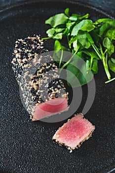 Fried tuna steak in black sesame with asparagus on black plate