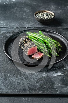 Fried tuna steak in black sesame with asparagus on black plate