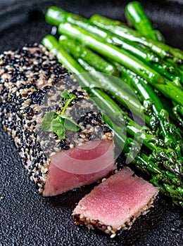 Fried tuna steak in black sesame with asparagus on black plate