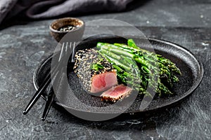 Fried tuna steak in black sesame with asparagus on black plate